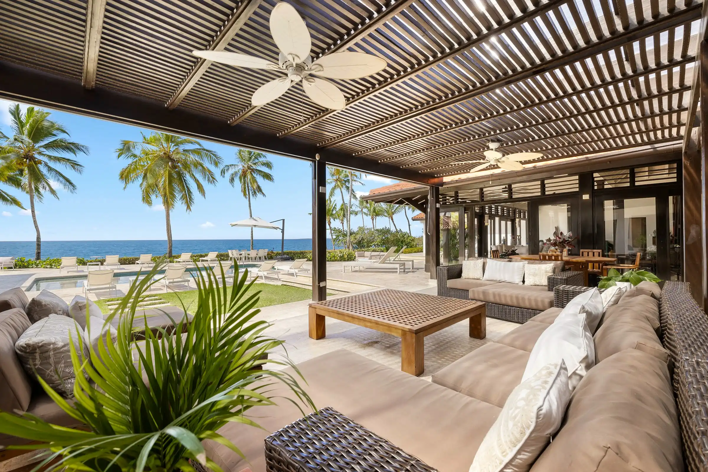 Covered outdoor lounge at Costa Verde 3 under a timber slatted roof, looking through palms to the Caribbean