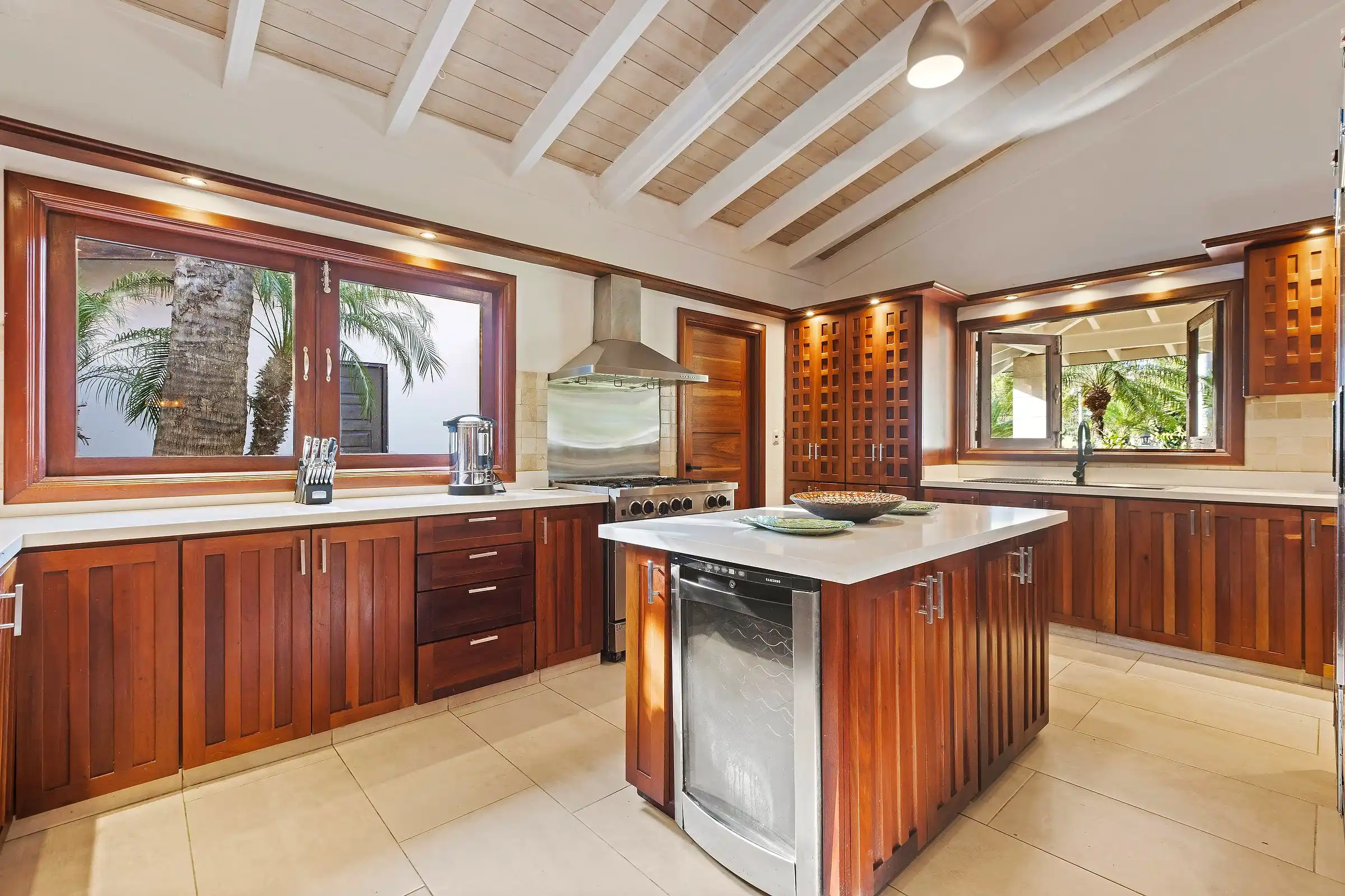 The kitchen island at Costa Verde 3 beneath walls of louvered light, hardwood cabinetry throughout