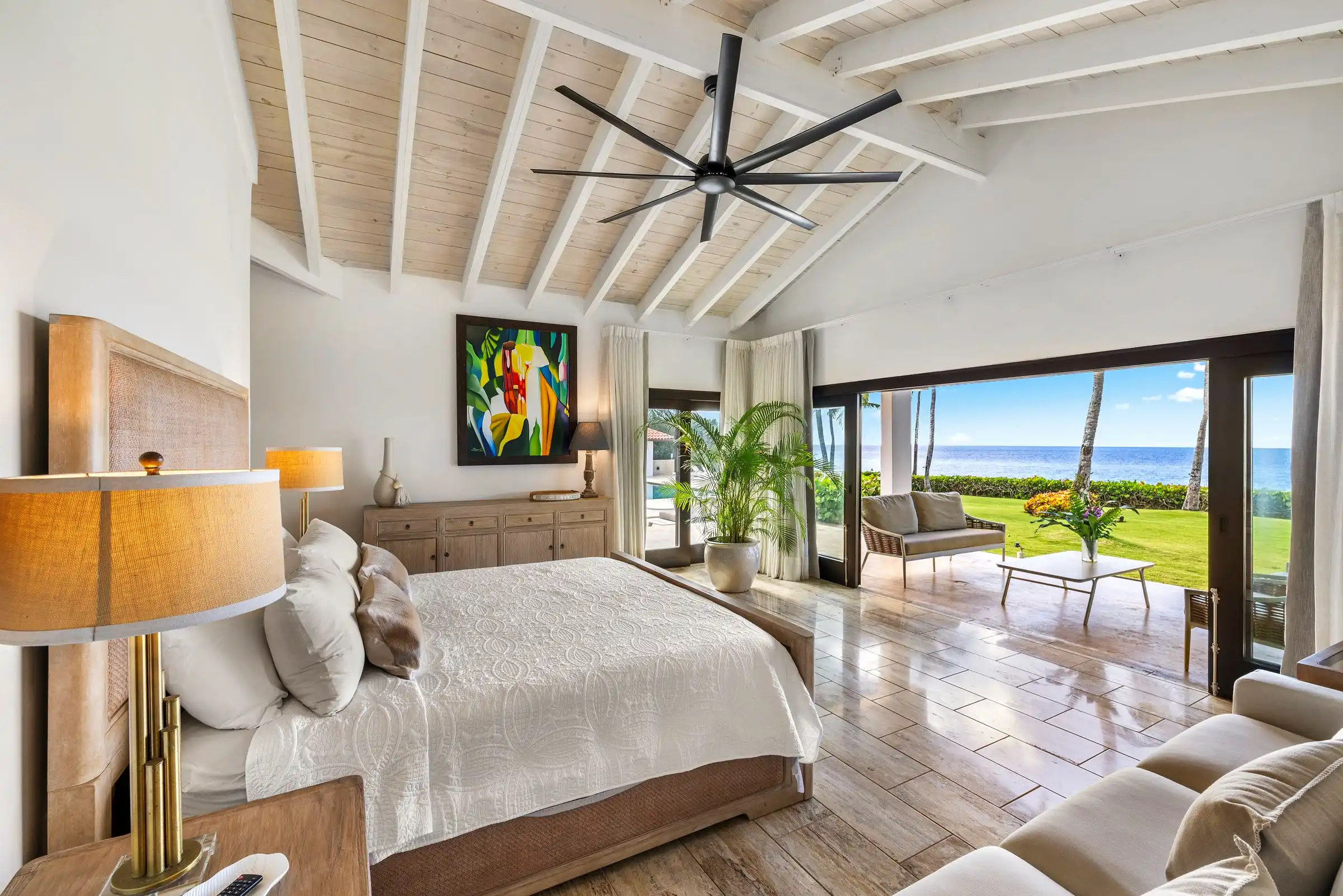 Ocean-view bedroom at Costa Verde 3 beneath a beamed ceiling, sliding doors open to the lawn and sea