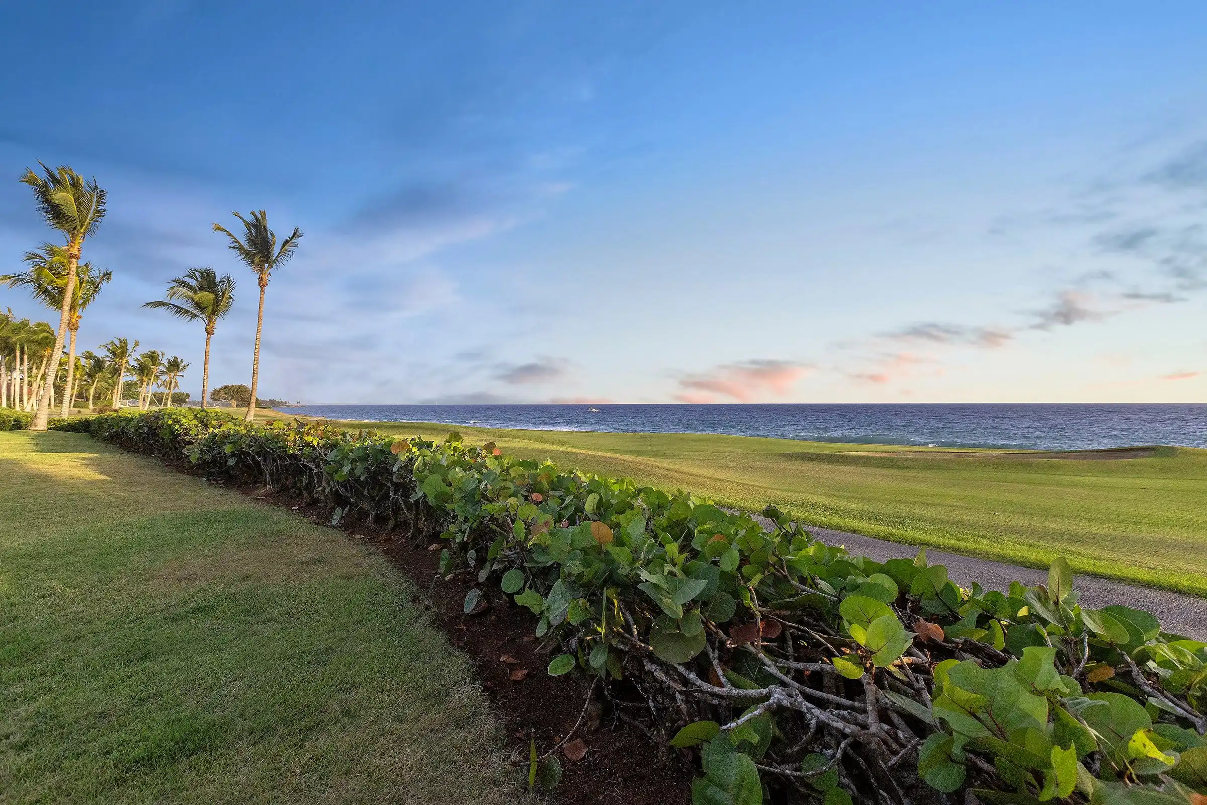 The ocean-front event lawn at Costa Verde 3 at dusk, running past the sea-grape hedge to the Caribbean — permitted for weddings and private events