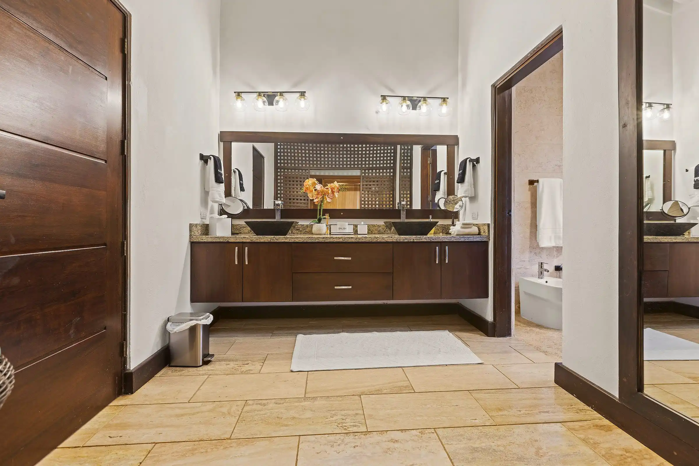 The primary bathroom at Costa Verde 3 with dual vanities in dark hardwood and stone floors