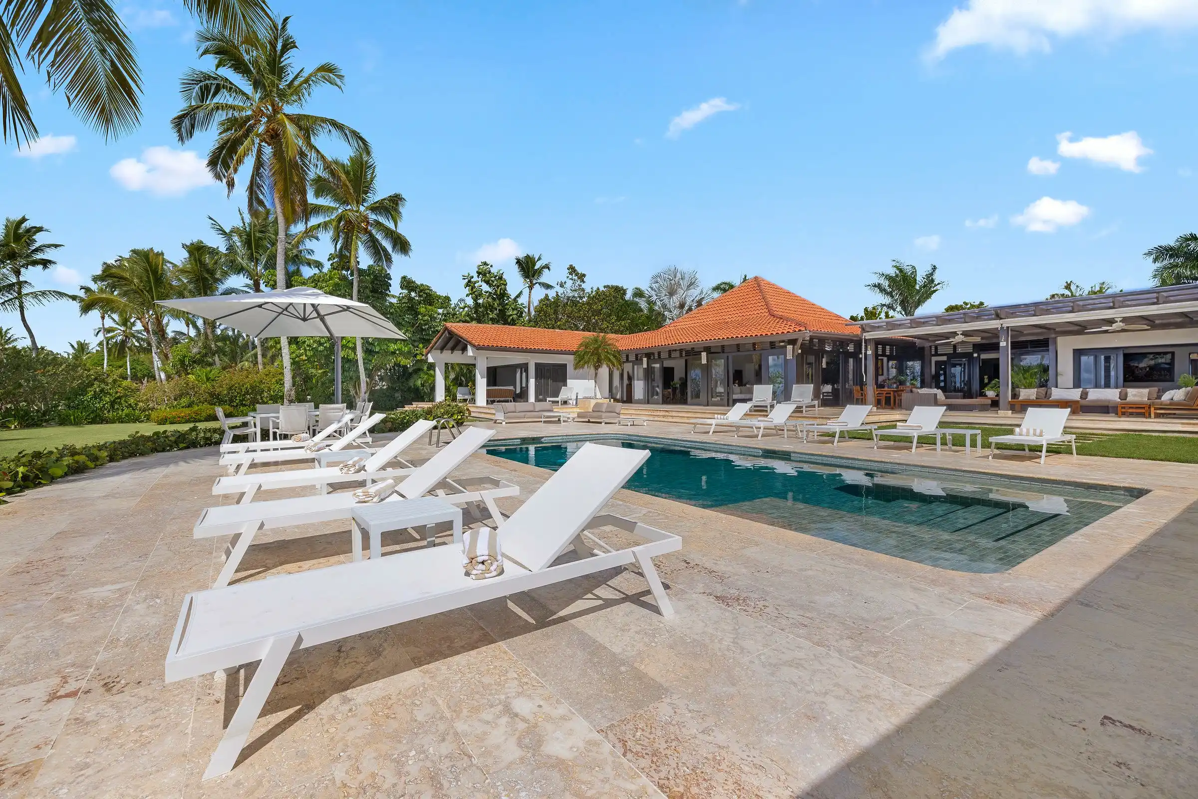 Sun loungers and a parasol beside the pool at Costa Verde 3, palms and the sea behind